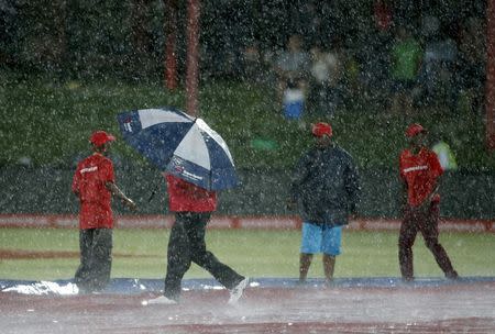 A worker holds an umbrella on the pitch after the first ODI cricket match between England and South Africa was stopped due to rain in Bloemfontein, South Africa, February 3, 2016. REUTERS/Siphiwe Sibeko