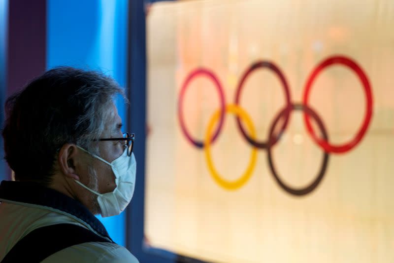 FILE PHOTO: A man wearing a protective face mask, following an outbreak of the coronavirus, stands in front of The Tokyo Olympic flag 1964 at The Japan Olympics museum in Tokyo