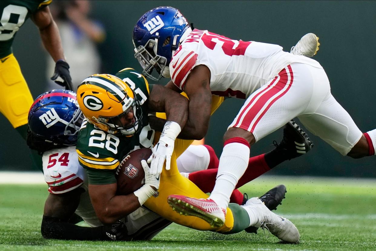 Green Bay Packers running back A.J. Dillon (28) is tackled by New York Giants linebacker Jaylon Smith (54) and safety Xavier McKinney (29) during the second half of an NFL football game Oct. 9, 2022, at Tottenham Hotspur Stadium in London.