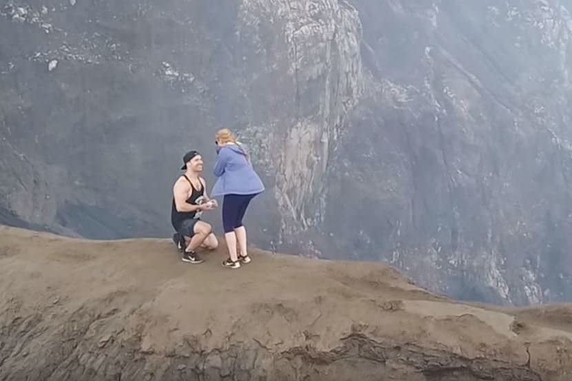 A travel blogger has reached dizzy new heights in the romance stakes, proposing to his partner at the top of a 7,600ft active volcanoCanadian couple, Alison and Jarod, were climbing their first volcano – Mount Bromo in Indonesia – when Jarod decided to pop the question.After trekking up the side of the volcano, the pair finally reached the peak and began walking along its narrow ridge. Footage taken by a drone owned by the romantic explorer and operated by their friend, then reveals the moment Jarod springs the surprise proposal on Alison.Jarod can be seen dropping to one knee and presenting Alison with the engagement ring, before she covers her mouth in shock and the pair embrace.Footage shows a stunned Alison covering her mouth in shock, before flinging her arms around her new fiancée. In an online statement accompanying the footage, Jarod wrote: “While walking atop the crater rim, hearing the deep rumble down below and stunning 360 landscape views, I got down on one knee and asked the love of my life to marry me. “She was so shocked and couldn't believe it was really happening. After some tears of joy, a big “YES”, and some kisses, Alison quickly said she needed to get off the volcano as she couldn't process both of these things happening at the same time. “We feel so lucky to have found each other in this adventure called life and there is no one else we'd rather be beside. Thanks to our friends Jenny and Stu for capturing the moment and helping make this all happen!The couple met on a teacher education programme in Ottawa and have reportedly been inseparable since.The pair now run a travel blog together called Our Moving Roots, which is inspired by the concepts of dynamism and positivity: “Our Moving Roots is the idea that in life we are not meant to be stagnant, but rather be in constant motion; planting new roots in the places we go, the people we meet, the experiences we have, while infusing love in all of the above,” it reads.