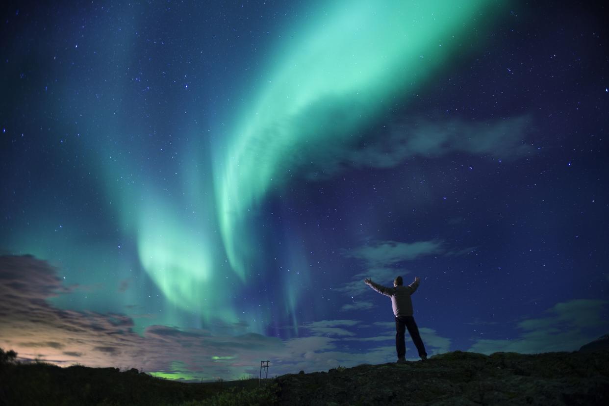 Dramatic aqua and blue aurora borealis over southern Iceland, person with arms stretched out standing, watching it, with bits of lime green and lavender purple