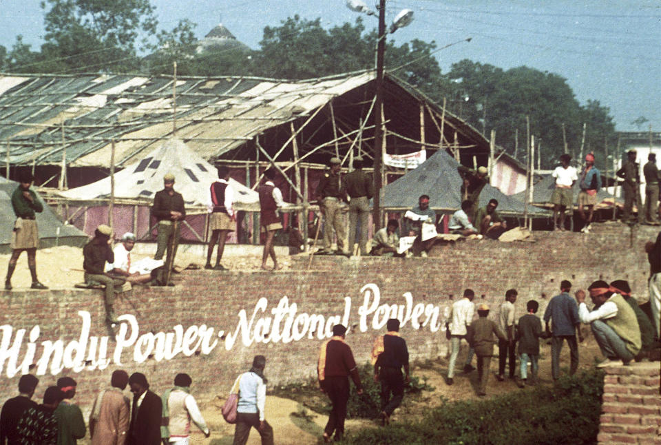 FILE - Hindu fundamentalists walk along the perimeter wall of the disputed site of a Ram temple to be built where the Babri mosque, at rear behind trees, still stood when this picture was taken in Ayodhya, Dec. 6, 1992. Later on militant Hindus stormed the 430-year old Muslim mosque and destroyed it. In 2019, India’s Supreme Court ruled in favor of building a Hindu temple on the disputed site. Hindus believe their god Ram was born there and say the Muslim Emperor Babur built a mosque on top of a temple at the site. (AP Photo/Udo Weitz, File)