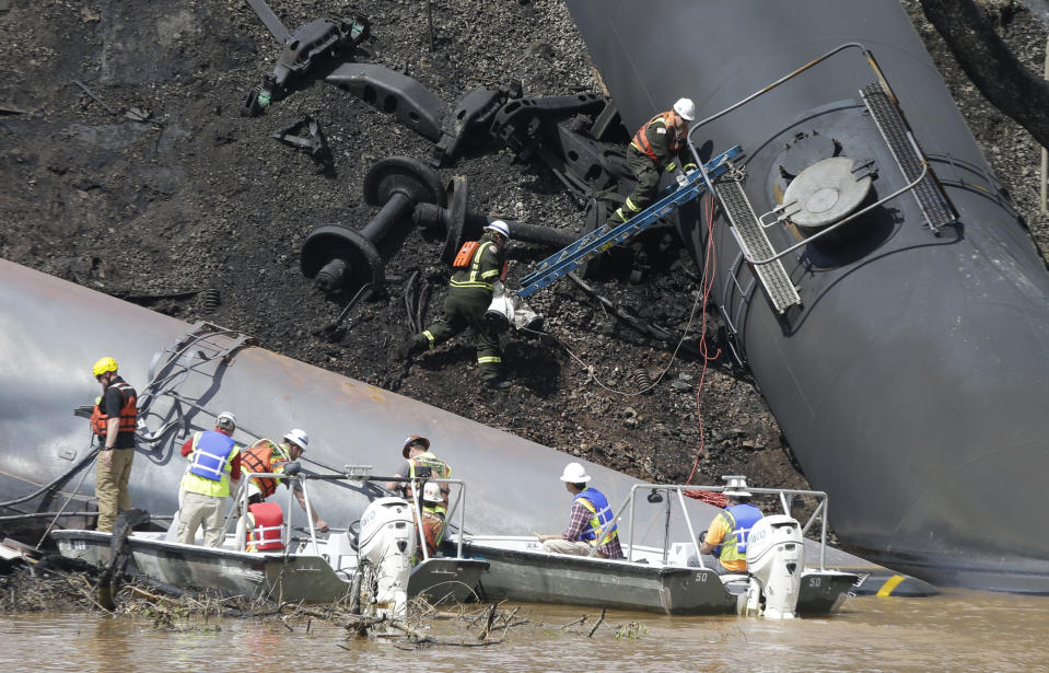 Workers remove damaged tanker cars along the tracks where several CSX tanker cars carrying crude oil derailed and caught fire along the James River near downtown Lynchburg, Va., Thursday, May 1, 2014. Department of Environmental Quality spokesman Bill Hayden said state workers smelled oil downstream from the derailment site during a night-time survey. CSX crews and heavy equipment contractors worked to clear more than a dozen derailed train cars, some carrying crude oil. Two cranes were lifting derailed cars and moving them to a new track. (AP Photo/Steve Helber)