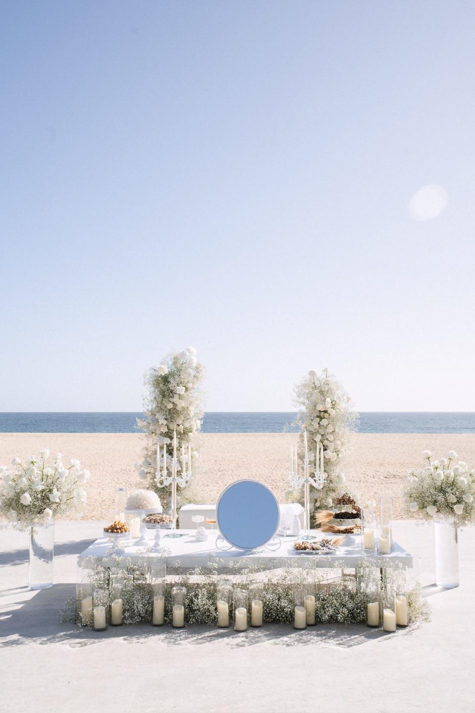 A floral arch and table sit in front of a beach and ocean.