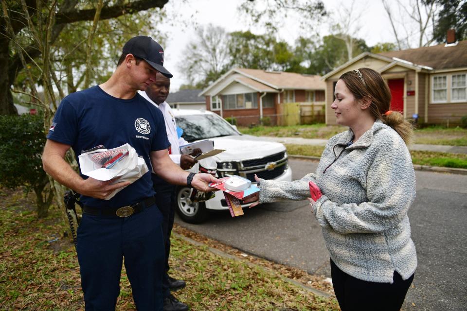 Firefighter Brent DeLoach (left) along with Chief Kevin Jones hands a free carbon monoxide detector to Christy Seckman. Fire officials were offering free smoke detectors as well to residents living near a house fire in the 1100 block of West 13th Street.