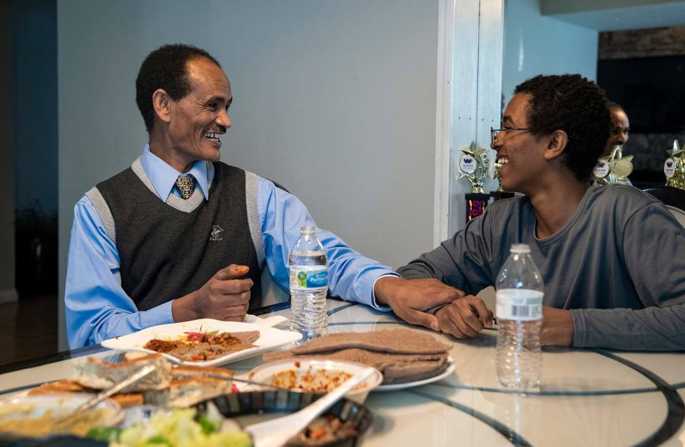 Mengsteab Aregay Gebremariam (left) and his 14-year-old son Mikias laugh over homemade family lunch, injera flatbread with various toppings.