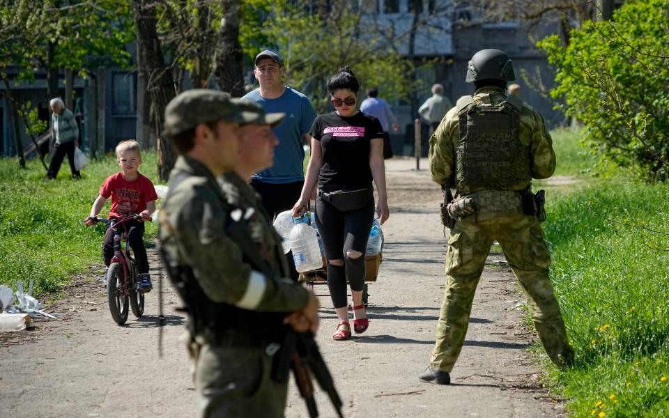 Serviceman of Donetsk People's Republic militia guard an area as local civilians walk to get humanitarian aid, bread and pure water distributed by Donetsk People Republic Emergency Situations Ministry in Mariupol, in territory under the government of the Donetsk People's Republic, eastern Ukraine, Friday, April 29, 2022. This photo was taken during a trip organized by the Russian Ministry of Defense. (AP Photo) - AP