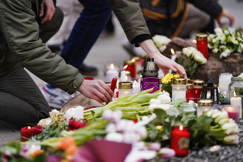 People lay flowers and candles by the wayside in front of a university building in Heidelberg, Germany, Jan. 25, 2022. On Jan. 24, 2022 an 18-year-old student stormed into the lecture hall of the building with a shotgun while the lecture was in progress and shot around. A young woman died, the perpetrator killed himself a little later. (Uwe Anspach/dpa via AP)