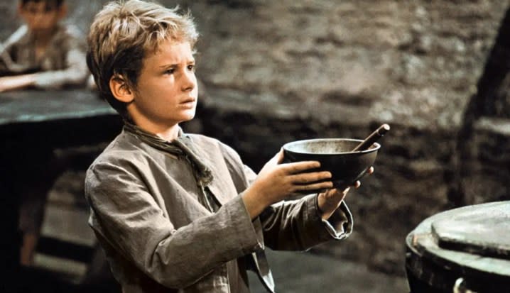 A young boy holds a bowl in his hands in Oliver!