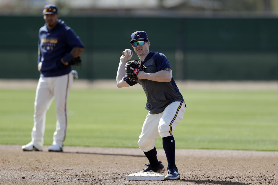 Milwaukee Brewers infielder Brock Holt throws to first as shortstop Orlando Arcia looks on, left, during spring training baseball Wednesday, Feb. 19, 2020, in Phoenix. Holt and the Brewers finalized a one-year contract Wednesday, a deal that includes a team option for 2021. (AP Photo/Gregory Bull)