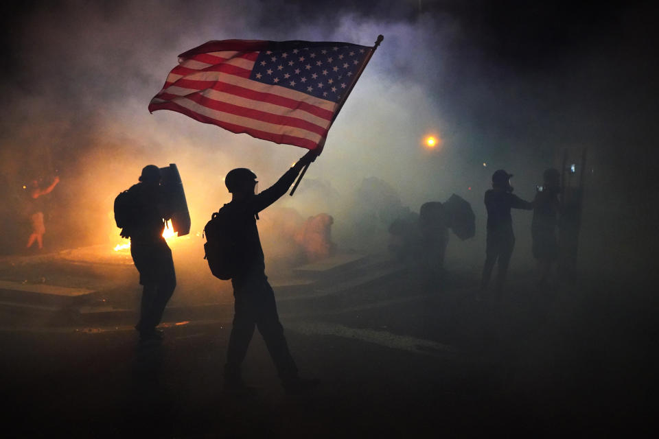 A protester holds an American flag aloft while walking through tear gas.