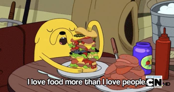 Animated character Jake from Adventure Time eating a large sandwich with text "I love food more than I love people."