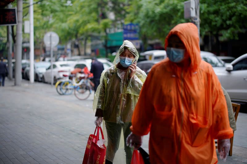 People wearing face masks and raincoats walk on a street in Wuhan