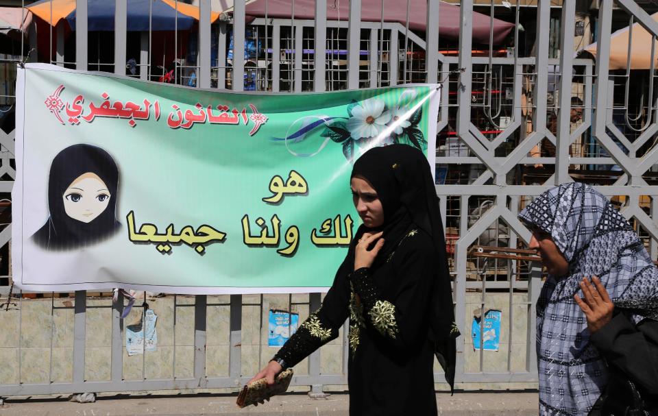 In this Thursday, March 13, 2014 photo, women pass by a banner for the Jaafari Personal Status Law in Baghdad, Iraq. The Arabic on the banner reads, "The Jaafari Personal Status Law is for you and all of us." The contentious civil status draft law for Iraqi Shiite community that allows child marriage and restricts women’s rights has stirred up a row among many Iraqis who see it as a setback for child and women rights, threatening to add more divisions and woos to the society that is already in fragments. (AP Photo/Karim Kadim)