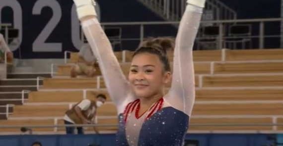 Suni Lee raising her arms after landing