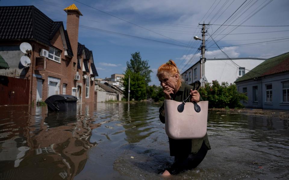 A local resident makes her way through a flooded road after the walls of the Kakhovka dam collapsed overnight - Evgeniy Maloletka/AP