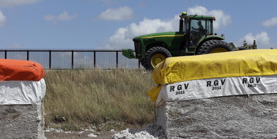 In this Sept. 6, 2012, photo, a tractor is used to farm in cotton field along a U.S.-Mexico border fence that passes through the property in Brownsville, Texas. Since 2008, hundreds of landowners on the border have sought fair prices for property that was condemned to make way for the fence, but many of them received initial offers that were far below market value. (AP Photo/Eric Gay)