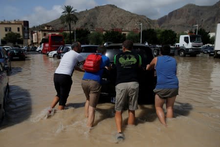 People push a car through a partially submerged parking as torrential rains hit Orihuela