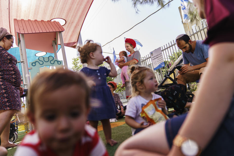 Rivi Abramowitz, background center, holds her daughter, Ori, 1, on the playground of a Torah Nucleus Jewish school in the mixed Arab-Jewish town of Lod, central Israel, Thursday, May 27, 2021. "We are observant from the religious Zionist community. I don't see why we're put into the rubric of 'settlers,'" said Abramowitz, who has lived in Lod for six years with her husband, who was born in town and whose parents were among the founders of the Torah Nucleus. "Nobody has come to throw out anybody." (AP Photo/David Goldman)