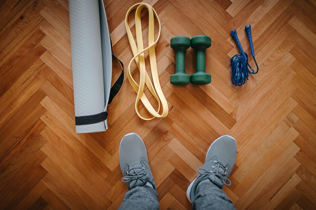 Low section of man with exercise mat, dumbbell, jump rope and resistance band on hardwood floor