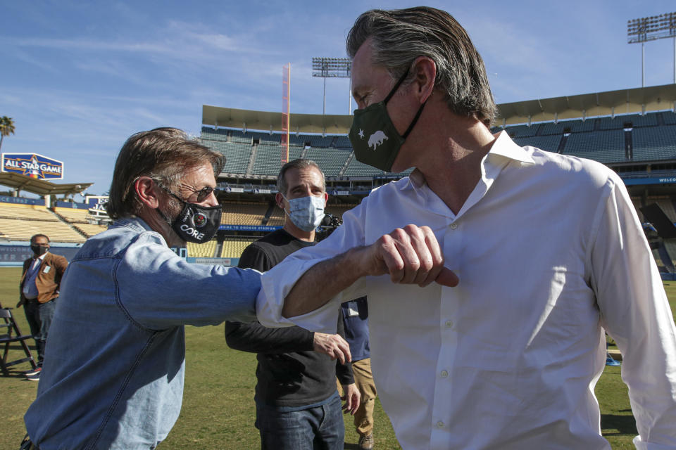 Actor Sean Penn, left, Los Angeles Mayor Eric Garcetti, back, and Governor Gavin Newsom, right, greet each other at a press conference held at the launch of a mass COVID-19 vaccination site at Dodger Stadium on Friday, Jan. 15, 2021, in Los Angeles. (Irfan Khan/Los Angeles Times via AP, Pool)