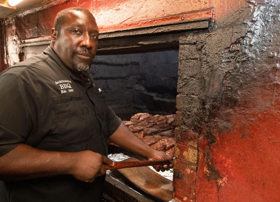 June 8, 2022; Northport, AL, USA; Woodrow Washington pauses at the barbecue pit as he turns slabs of ribs. Archibald’s Barbecue is celebrating 60 years of business. Gary Cosby Jr.-The Tuscaloosa News