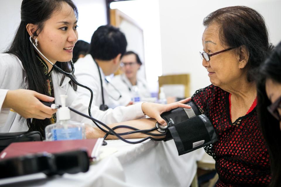 Two Asian women face each other - a young healthcare worker measures blood pressure of an older patient