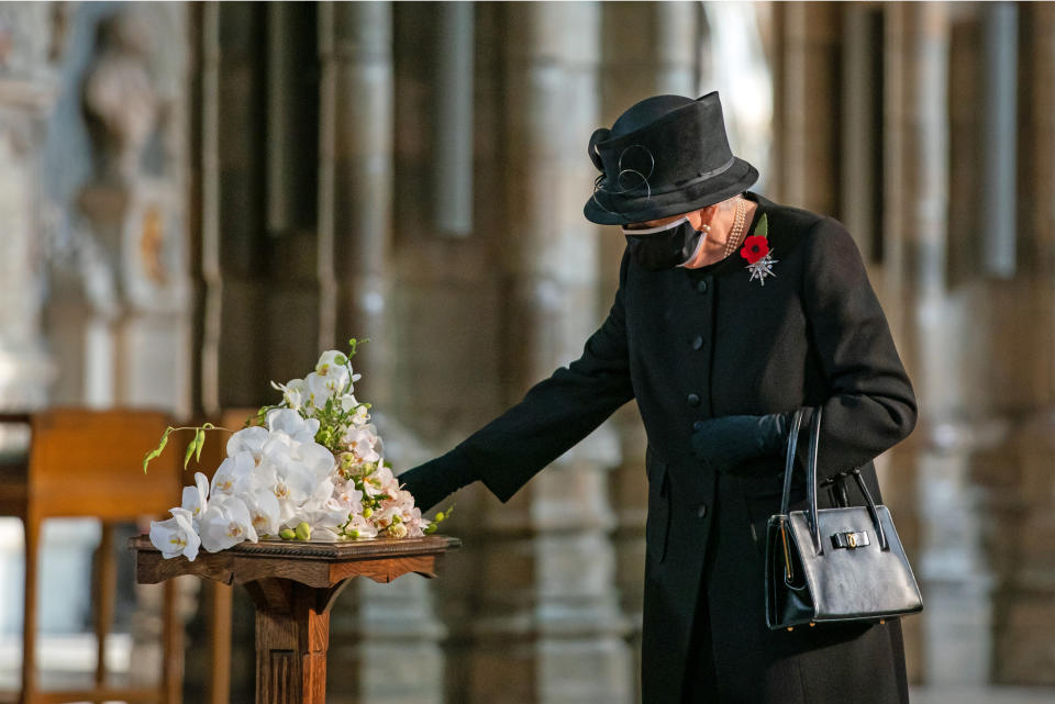 LONDON, ENGLAND - NOVEMBER 04: Queen Elizabeth II inspects a bouquet of flowers placed on her behalf at the grave of the Unknown Warrior by her Equerry, Lieutenant Colonel Nana Kofi Twumasi-Ankrah, during a ceremony in Westminster Abbey to mark the centenary of the burial of the Unknown Warrior on November 4, 2020. The grave of the Unknown Warrior is the final resting place of an unidentified British serviceman who died on the battlefields during the First World War and whose body was brought from Northern France and buried at Westminster Abbey on 11th November 1920. (Photo by Aaron Chown - WPA Pool/Getty Images)