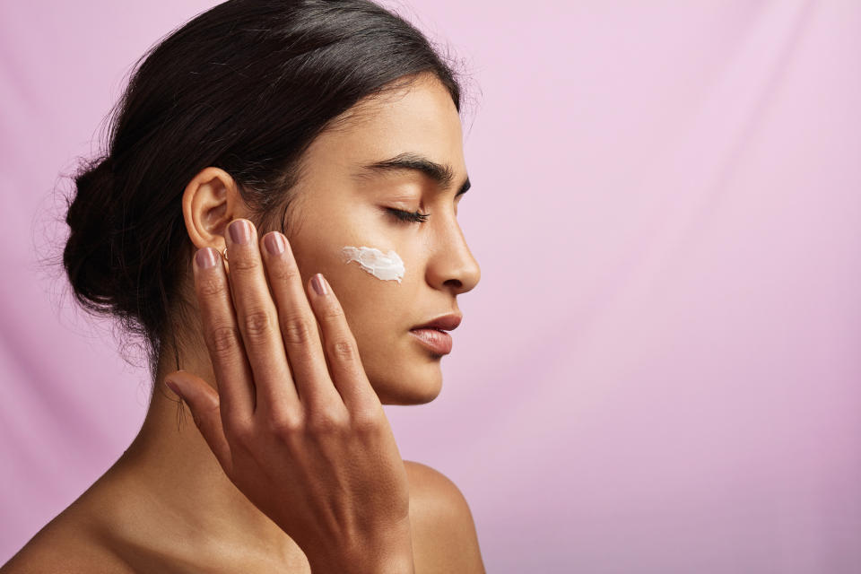 Studio shot of a beautiful young woman applying moisturizer to her face