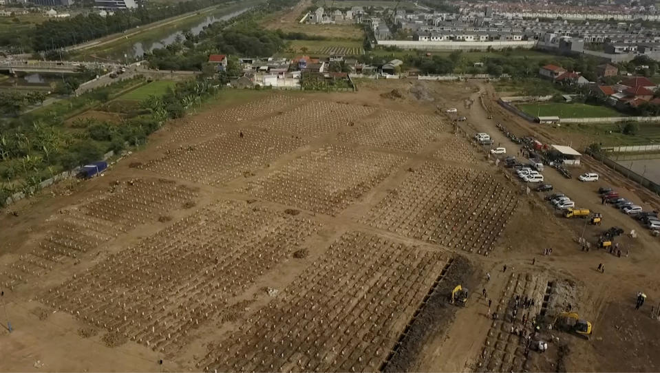 In this image from drone video, backhoes dig additional burial plots at the Rorotan cemetery, a graveyard built for COVID-19 victims in Jakarta, Indonesia on July 23, 2021. Indonesia surpassed the grim milestone of 100,000 official COVID-19 deaths on Wednesday, Aug. 4, 2021, as the country struggles with its worst pandemic year fueled by the delta variant, with growing concerns that the actual figure could be much higher with people also dying at home. (AP Photo/Andi Jatmiko)