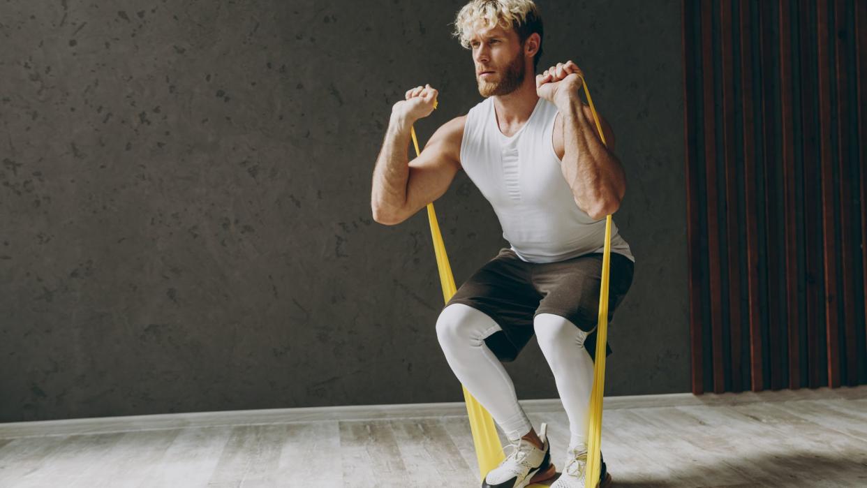  A man performing squats with a resistance band. 