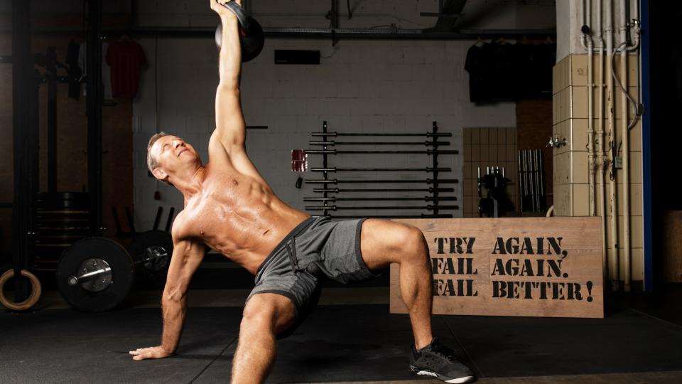 Man performing a Turkish get-up during workout with left arm extended holding a kettlebell and left leg bent and right leg extended