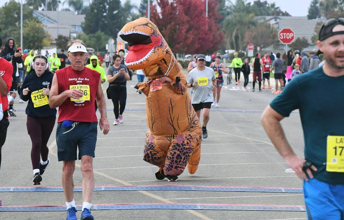 Kisha Xiong, in a dinosaur costume, finishes the 10K at the annual Two Cities Marathon, which started and finished at the Clovis Community College campus Sunday, Nov. 6, 2022, in Fresno.