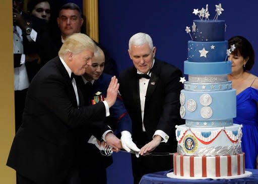 President Donald J. Trump, left, and Vice President Mike Pence, right, are helped by Coast Guard Petty Officer 2nd Class Matthew Babot, center, as they cut a cake at The Salute To Our Armed Services Inaugural Ball Friday, Jan. 20, 2017, in Washington. (AP Photo/David J. Phillip)