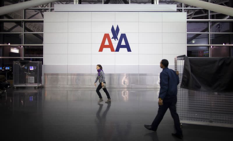 People walk past an American Airlines logo at John F. Kennedy (JFK) airport in in New York