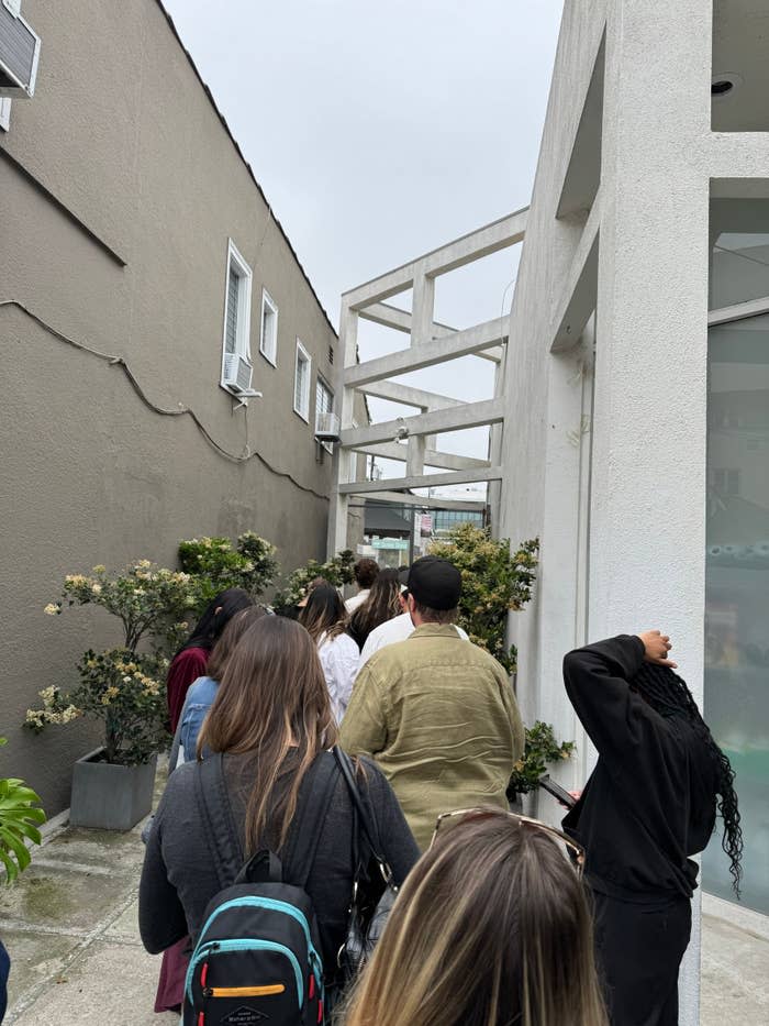 A group of people standing in line outdoors between two buildings.