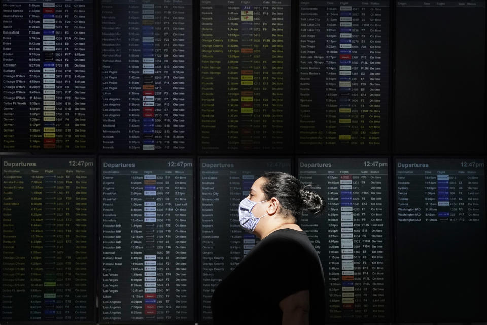 A woman wears a mask while walking past a flight information board at San Francisco International Airport during the coronavirus outbreak in San Francisco, Tuesday, Nov. 24, 2020. (AP Photo/Jeff Chiu)