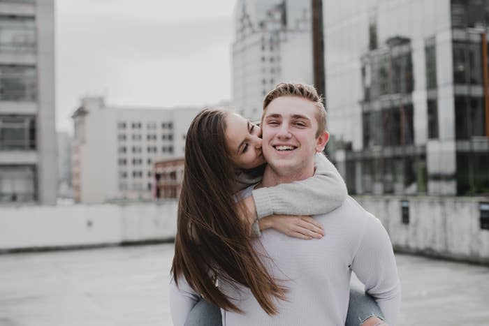 A boyfriend giving his girlfriend a piggyback ride on an urban rooftop