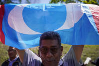 A supporter of People's Justice Party waves its party flag outside the National Palace in Kuala Lumpur, Malaysia, Wednesday, Feb. 26, 2020. Malaysia's ruling alliance collapsed this week after 94-year-old Prime Minister Mahathir Mohamad resigned and dozens of lawmakers defected in an audacious attempt to form a new government. The political earthquake occurred less than two years after the alliance won a historic election that ousted a corruption-tainted coalition that had ruled for 61 years. (AP Photo/Vincent Thian)