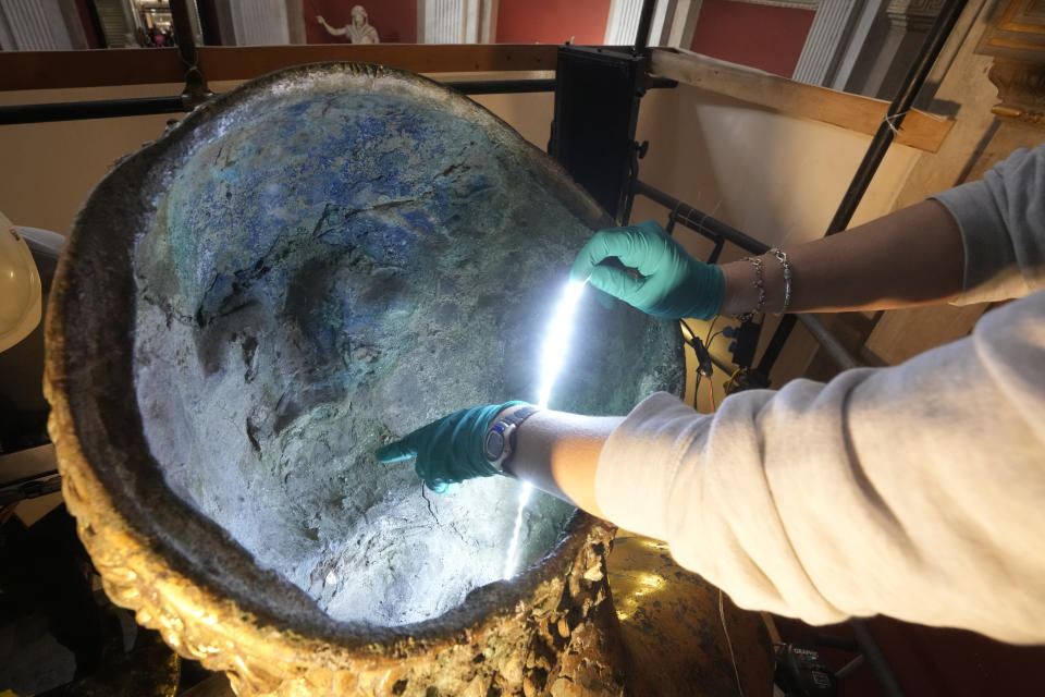 Vatican Museum restorer Alice Baltera points at the inside part of the Hercules statue, in the Round Hall of the Vatican Museums, Thursday, May 11, 2023. Work will continue until December to reveal the 4-meter- (13-foot-) tall Hercules, believed to have stood in ancient Rome’s Pompey Theater, to its original golden sheen. The discovery of the gilded bronze in 1864 during work on a banker’s villa near Piazza dei Fiori made global headlines. (AP Photo/Andrew Medichini)