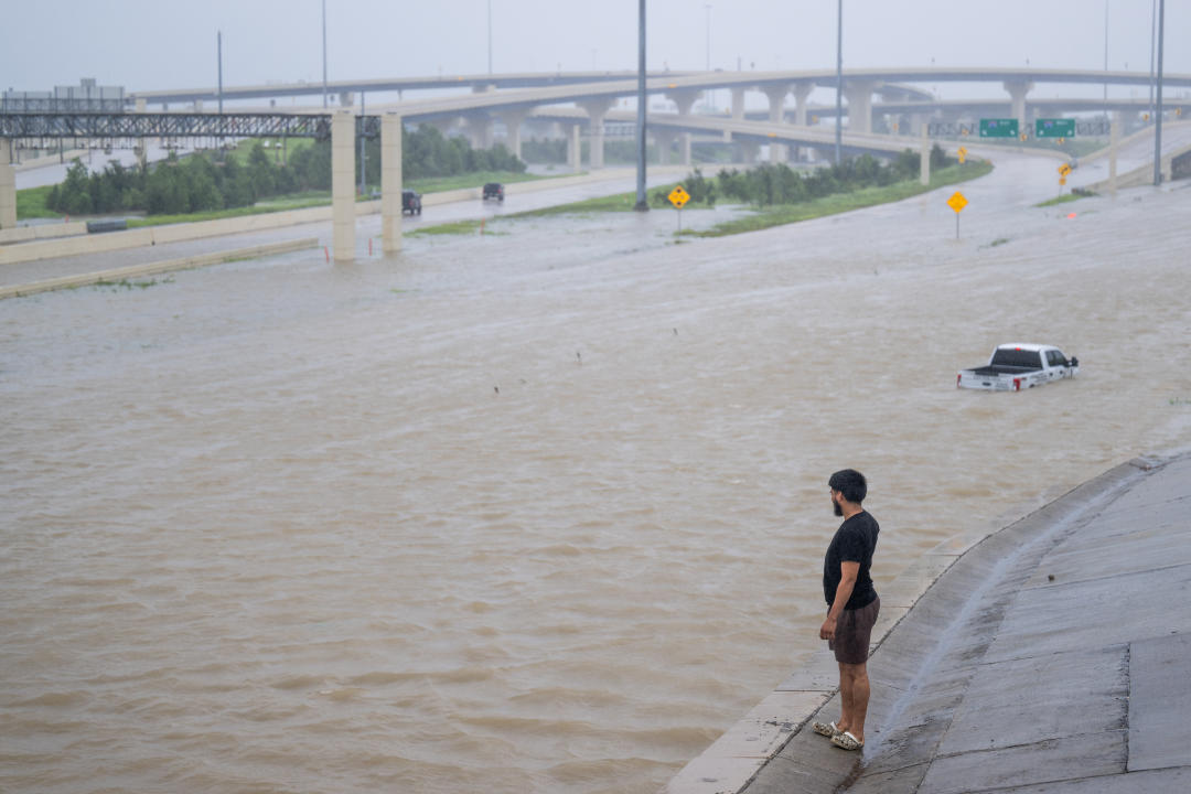 A person looks out toward a flooded interstate, with a half-submerged pickup truck in the distance.