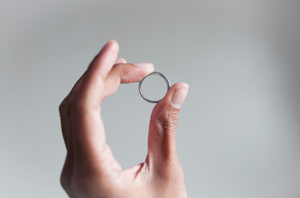 A hand holding a ring between thumb and middle finger