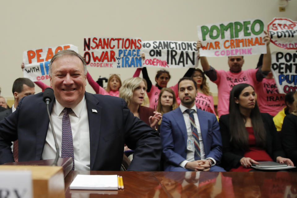 Protesters hold up signs as Secretary of State Mike Pompeo arrives to testify at a House Foreign Affairs Committee hearing on Capitol Hill in Washington, Friday, Feb. 28, 2020, about the Trump administration's policies on Iran, Iraq and the use of force. (AP Photo/Carolyn Kaster)