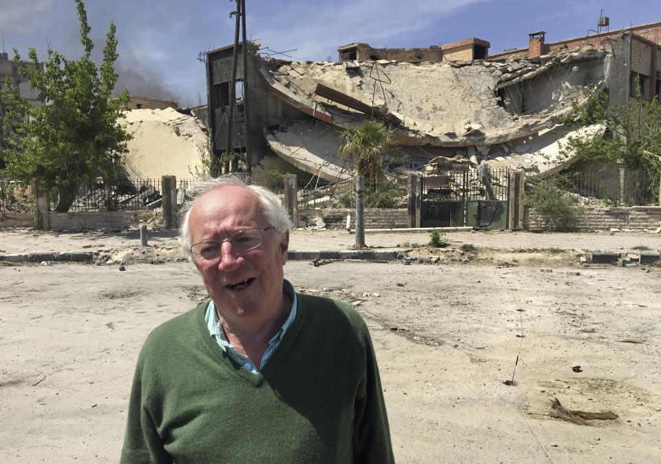 Veteran British journalist Robert Fisk stands in front of a damaged building in the Damascus suburb of Douma, during a tour by Syria's Information Ministry to the town days after it was captured from rebels by Syrian government forces, April 16, 2018. Fisk, one of the best-known Middle East correspondents who spent his entire career reporting from the troubled region and won accolades for challenging mainstream narratives died Sunday at a hospital in Dublin after a short illness. He was 74. (AP Photo/Bassem Mroue)