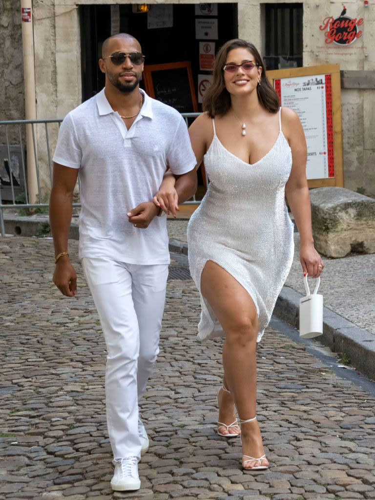Ashley Graham, in a shimmering short dress, and husband Justin Ervin, in light-colored pants and shirt, arrive at the Hotel de la Mirande