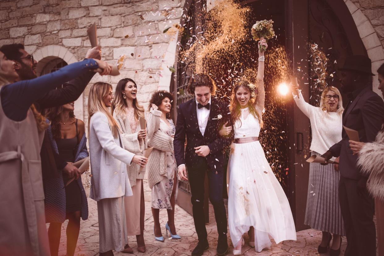 Newlywed bride and groom leaving church and celebrating wedding with guests throwing flowers and rice