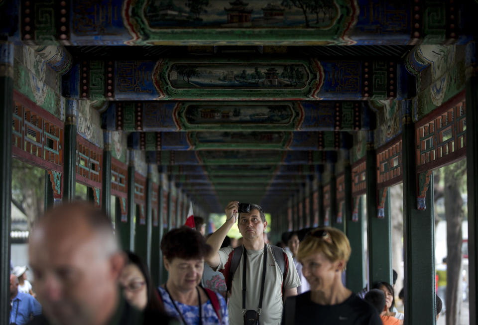 In this Wednesday, Aug. 28, 2013 photo, a tourist takes pictures as he and others walk down a corridor adorned with thousands of paintings depicting landscapes, birds and flowers at the Summer Palace in Beijing. China's new tourism slogan "Beautiful China" has been criticized by industry experts who say it illustrates a marketing problem that has led to a weakness in growth in foreign visitors over the past few years. (AP Photo/Andy Wong)