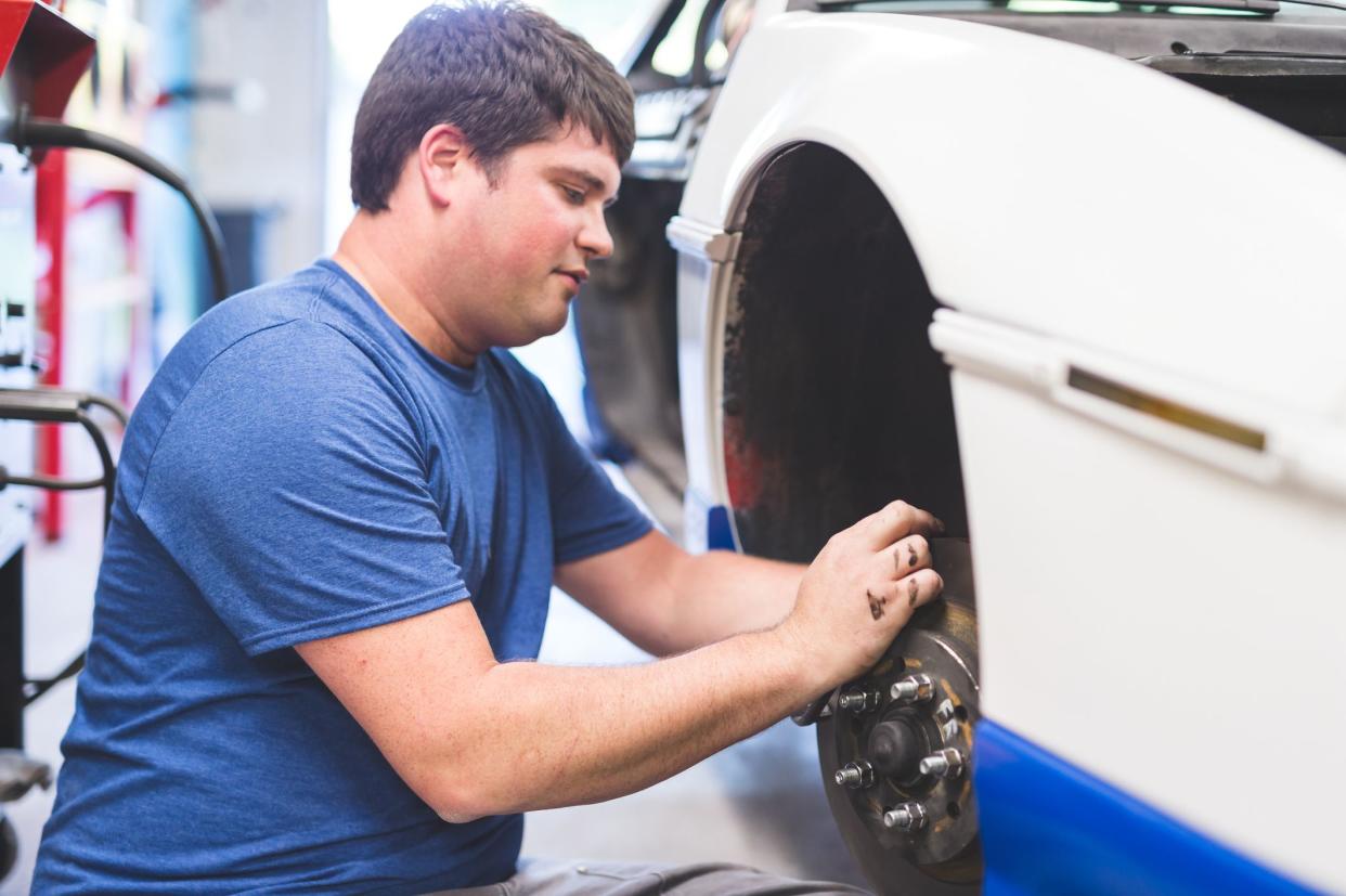 Mechanic works on car in his home garage. He is working on the wheels and rotors and has the tires off.