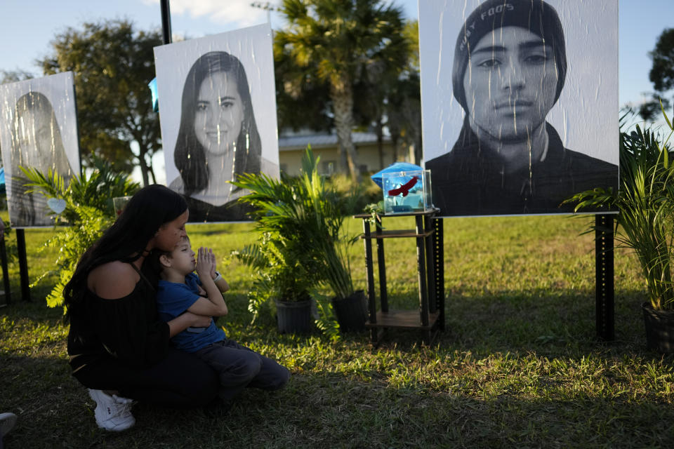 Mariana Rocha and her son Jackson Laparl, 6, visit a portrait of Rocha's cousin Joaquin Oliver, right, part of a display of portraits of the 17 students and staff of Marjory Stoneman Douglas High School who were killed, during a community commemoration on the five-year anniversary of the shooting, Tuesday, Feb. 14, 2023, at Pine Trails Park in Parkland, Fla. Family members, neighbors and well wishers turned out to multiple events Tuesday to honor the lives of those killed on Valentine's Day 2018. (AP Photo/Rebecca Blackwell)