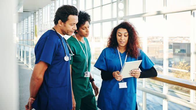 Three doctors in scrubs looking at digital tablet and discussing.